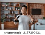 Small photo of Active sporty lifestyle. Happy asian mature man holding resistance bands hang around his neck, resting after domestic workout, standing in living room