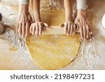 Hands of european small girl and elderly grandmother make dough with rolling pin for pizza and cookies in kitchen interior, top view. Lesson of cook homemade food together, family enjoy prepare baking