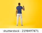 Small photo of Back View Of African American Man Pointing Finger Up Pushing Invisible Button Or Touchscreen Standing Over Yellow Studio Background. Look Upward. Full Length Shot