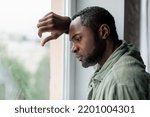 Small photo of Unhappy frustrated adult african american guy in casual suffering from depression and bad news near window in home interior. Health problems, stress from self-isolation during covid-19 quarantine