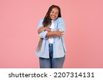 Small photo of Body Positive. Happy African American Overweight Female Hugging Herself Posing With Eyes Closed, Wearing Plus Size Clothes Standing Over Pink Studio Background. Self Love Concept