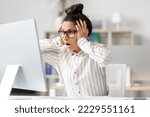 Business problem. Shocked female entrepreneur looking at computer monitor and touching head, reading awful news online, sitting in office. Entrepreneurship issues concept