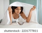Small photo of Beautiful brunette short-haired young lady doing facial streaming procedure at home, sit at vanity table above bowl with hot water and essential oils, cover head with bath towel. Domestic skin care