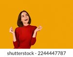 Dreamy excited beautiful brunette young woman in red snap fingers and looking at copy space over orange studio background, making dreams come true, waiting for mirracle