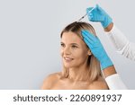 Small photo of Beautician injections for healthy hair growth. Mesotherapy of the scalp. Middle aged woman undergoing course of spa treatments for healthy strong hair, isolated on studio background, copy space