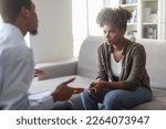 Small photo of Unhappy black millennial woman with bushy hair in casual sitting on couch, listening to psychotherapist african american man in formal outwear, female fighting with addiction. Psychological support