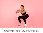 Small photo of Beautiful Sporty Young Woman Doing Deep Squat Exercise Over Pink Background In Studio, Motivated Millennial Female Making Fitness Training Indoors, Enjoying Healthy Lifestyle, Copy Space