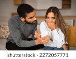 Small photo of Sad angry millennial arab guy shows smartphone to european woman in interior room, close up. Quarrel, app of social networks chat and blog, gadget addiction, treason online and relationships problems