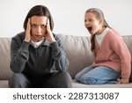 Small photo of Angry excited aggressive teenager european girl yelling at sad tired millennial woman in living room interior. Relationship problems between mother and daughter, quarrel, hysteria