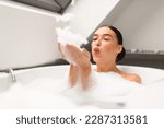 Relaxed Woman Blowing Foam Having Fun Taking Bath Sitting In Bathtub Full Of Hot Water With Soap Bubbles In Bathroom At Home. Lady Enjoying Hygiene Routine Bathing Indoor. Selective Focus
