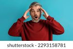 Small photo of Shocked appalled middle aged grey-haired man wearing casual gesturing on blue background, touching his head and exclaiming, panorama. Human gestures and emotions concept