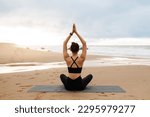 Small photo of Outdoor yoga. Woman meditating with hands clasped above head, sitting in lotus position on fitness mat on beach, practicing meditation near ocean, back view