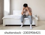 Small photo of Financial stress: Sad unhappy middle aged asian man wearing pajamas sitting on bed at home, touching head, worried about financial situation, struggling with debt, unemployment, unexpected expenses