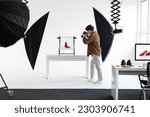 Framing the perfect shot. Male photographer taking photos of red shoes, working in modern photostudio, making content photoshoot, full length shot