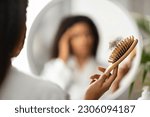 Small photo of Hairloss Concept. Upset Black Woman Holding Comb Full Of Fallen Hair After Brushing, Closeup Shot Of African American Female With Brush In Hand Standing Near Mirror, Suffering Alopecia Problem