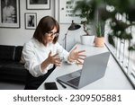Angry frowning young businesswoman working online on laptop pc computer, getting video call or reading emails and gesturing, sitting at coworking space, copy space