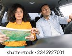 Small photo of Road Navigation Issue. Perplexed Arab couple riding car holding and pointing at map choosing route and having problems navigating vehicle, sitting in automobile, view from dashboard