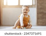 Adorable happy blonde infant baby playing with kids toys at home while sitting on carpet floor in living room. Portrait of smiling cute child toddler using colorful toys, copy space