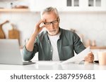 Home Office Paperwork. Portrait Of Senior Gentleman At Kitchen Desk, Reviewing Documents And Using Laptop, Elderly Man Engaged In Remote Work, Reading Financial Papers At Home, Free Space