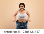 Small photo of Slimming Concept. Happy Slim Indian Woman Wearing Oversized Jeans Posing On Beige Background, Smiling Female With Drawn Fat Silhouette Around Body Comparing Size After Effective Weight Loss, Collage
