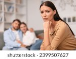 Small photo of Upset young woman on couch caught in love triangle, looking at camera unhappily, suffering from jealousy while friend man hugging girlfriend, sitting in living room indoor. Betrayal and jealousy