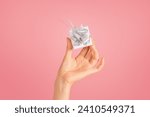 Small photo of Delicate lady hand holding a small, white gift with a shimmering silver bow, conveying a sense of care, surprise, and generosity on a smooth pink backdrop, cropped, ad and offer