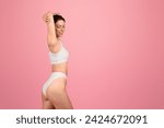 Small photo of Content and composed, european young woman with closed eyes raises her arms above, showcasing a serene moment in a snug white sports top and bikini on a pink background, studio