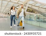 Small photo of Young couple in rush running with yellow suitcase at the airport, happy millennial man and woman laughing and enjoying the start of their vacation, rushing to flight boarding, copy space