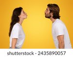 Small photo of Side profile of european young man and woman in white t-shirts facing each other with puckered lips on a bright yellow background, suggesting a playful interaction, studio
