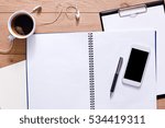 Notepad, diary, mobile phone and espresso coffee. Office or student's devices on modern wooden desk. Working table top view. Education or job background with copy space on paper sheet
