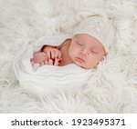 Newborn baby boy sleeping on white fur background wearing rnitted hat. Sweet studio photoshoot of cute infant child