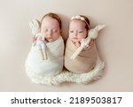 Small photo of Newborn babies twins swaddled in fabric sleeping on fur. Infant child kids brother and sister studio photoshoot