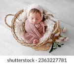 Small photo of Adorable newborn baby girl lying in basket with peony flowers decoration portrait. Cute infant child kid swaddled in fabric sleeping