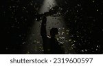 Small photo of Silhouette of race car driver celebrating the win in a race against bright stadium lights, rising a trophy over his head