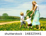 Mother and two children, a baby and a small child  holding hands and dancing and playing outside in a field of Flowers.