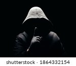 Photo of a scary horror man in hoodie showing silence hand sign in dark.