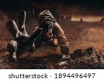 Photo of a dying stalker in jacket and gloves in damaged gas mask with filter reaching out his hand to camera on destructed apocalyptic wasteland city background.