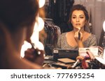 Brunette woman applying make up (paint her skin) for a evening date in front of a mirror. Focus on her reflection