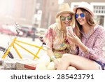 A picture of two girl friends using smartphone while riding tandem bicycle