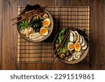 Small photo of Traditional ramen with jerked pork or chicken. With udon or ramen noodles. Served in classic bowls. Gyoza dumplings and mushrooms in the background. Natural wooden background.