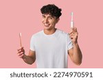 A young man compares manual vs electric toothbrush for optimal dental care - weighing effectiveness, convenience, and cost.
