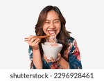 Happy young Asian woman eating noodles with chopsticks.
