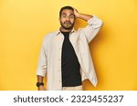 Casual young Latino man against a vibrant yellow studio background, being shocked, she has remembered important meeting.