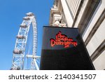 Small photo of London, UK - 26th March 2022: Entrance to the London Dungeon, with the London Eye against a blue sky background. Two of the popular London tourist attractions on the Southbank.