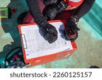 Top view of an unrecognizable marine biologist writing data on a paper on a boat