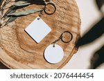 Small photo of Keychain mockup among olive leaves to display design. Blank white sublimation key chain photo. Flat lay, top view.
