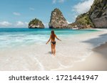 Back view young slim woman weaing black bikini  with long dark hair  on a tropical beach enjoy summer vacation. Vacation in Nusa Penida