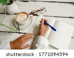  Female hads writing on paper notebook near cup of coffe and glasses. Young woman student writes information from portable net-book while prepare for lectures