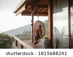 Tourist woman swing on wicker rattan hang chair in the jungle, nature mountains view, hold in hands cup of tea/coffee