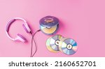 Small photo of Personal compact portable CD player disks purple headphones on a pink background. Top view layout, copy space, place for text or advertising. Hobby entertainment leisure